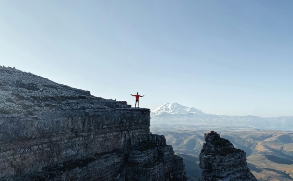 Man with his arms up standing at the top of a mountain